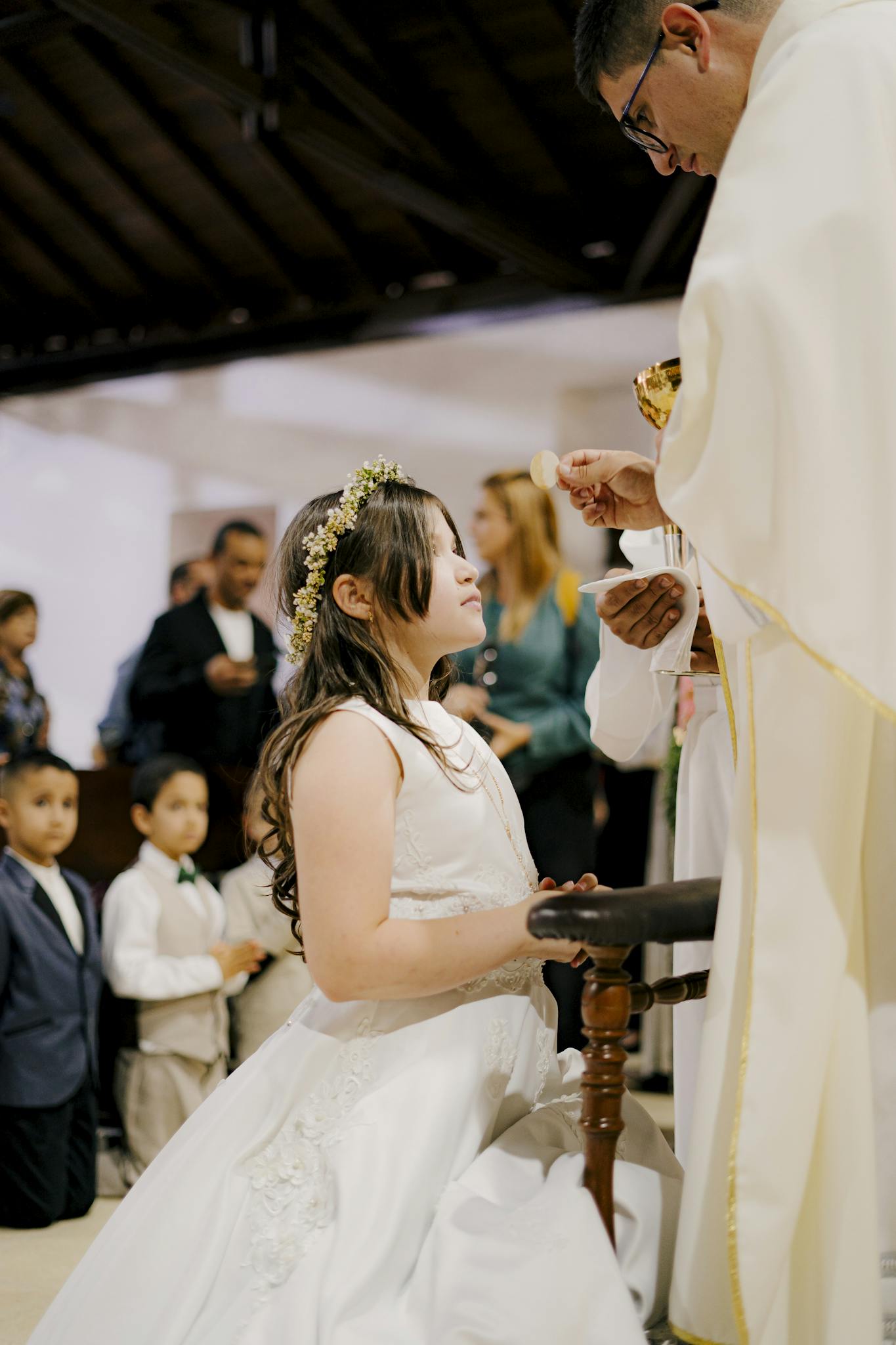 A young girl in a white dress participates in a First Communion ceremony inside a church.